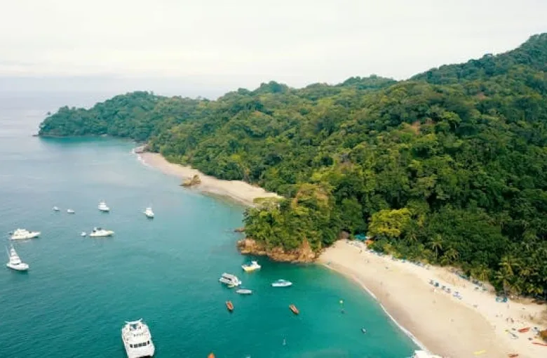 A curving Costa Rican beach with small boats offshore and forest running to the sand.