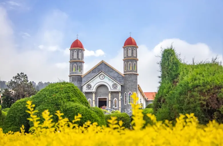 A whitewashed church with red domes above a garden of clipped topiary in Costa Rica.