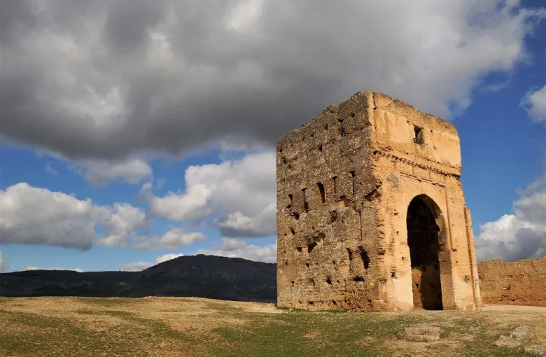 A weathered stone gateway standing alone on a green plain under a cloudy sky.