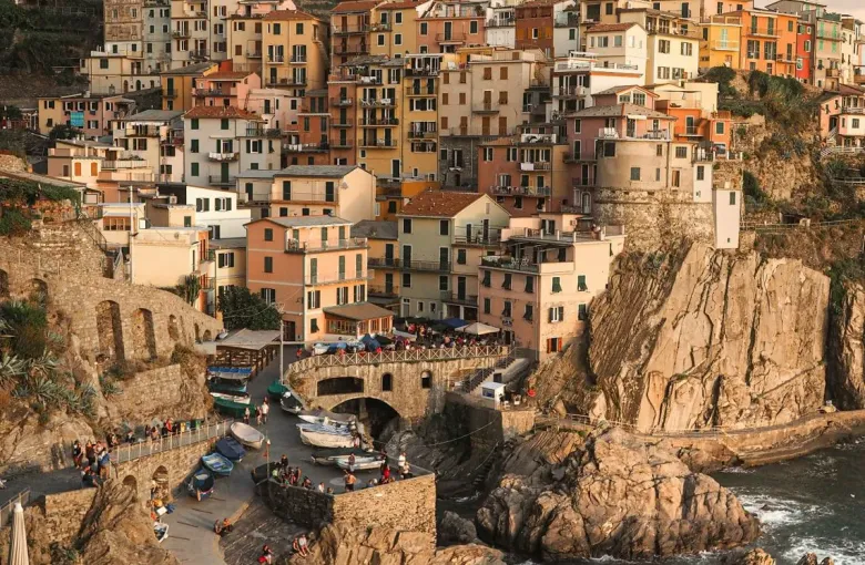 Pastel houses stacked up a steep cliff above a small rocky harbor in an Italian coastal village