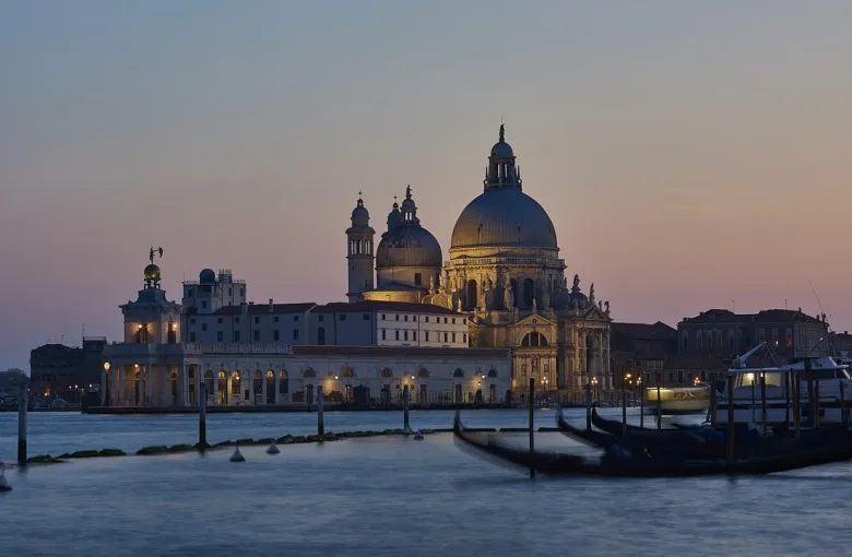 A domed basilica across the water at dusk, with moored gondolas in the foreground, Venice