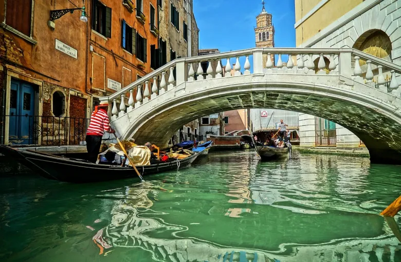 A gondolier steering under a stone bridge on a narrow Venetian canal