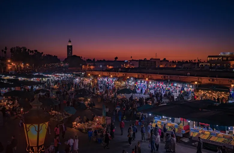 Food stalls and crowds filling Jemaa el-Fna square in Marrakesh at dusk, the Koutoubia minaret lit behind.