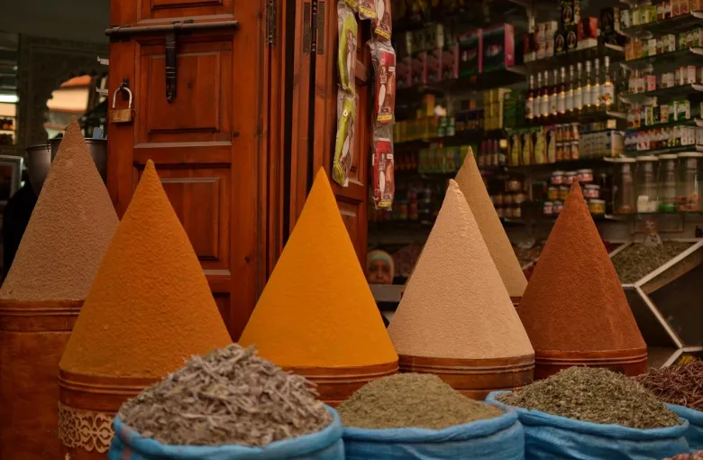 Cones of colored ground spices stacked in open sacks at a Moroccan souk stall.