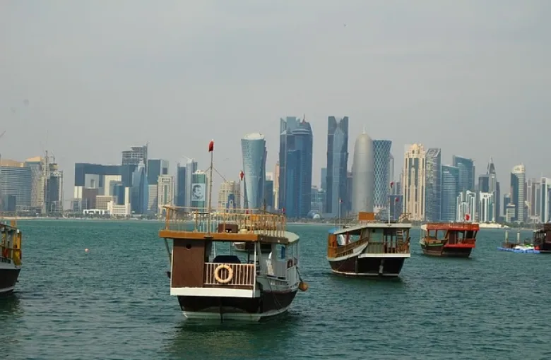 Traditional wooden dhow boats moored on the water in Doha, with the city skyline behind.