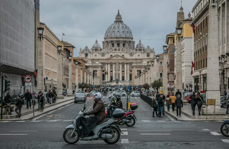 Saint Peter's Basilica at the end of a busy Rome street, with scooters and traffic in the foreground