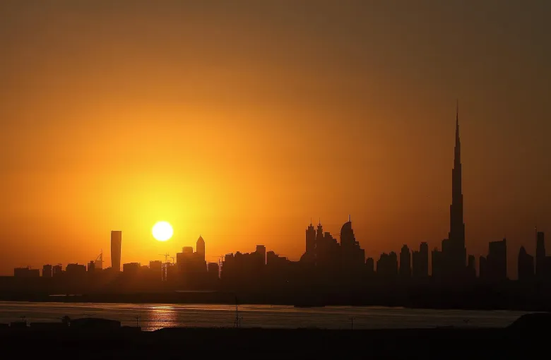 The Dubai skyline in silhouette against an orange sunset.
