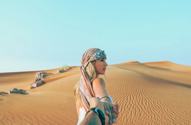 A woman in a headscarf standing among desert dunes near Dubai.