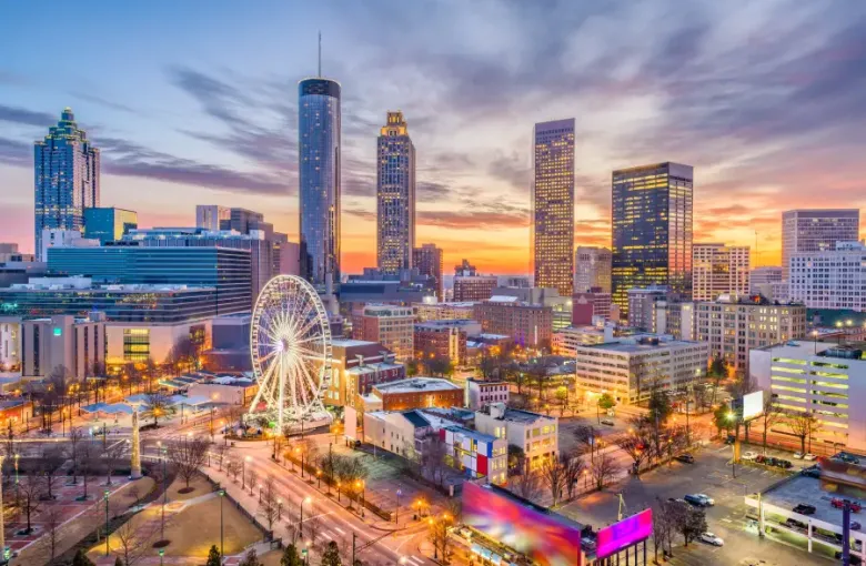 Atlanta Georgia downtown skyline at sunset with glowing skyscrapers a lit Ferris wheel and warm orange and purple sky