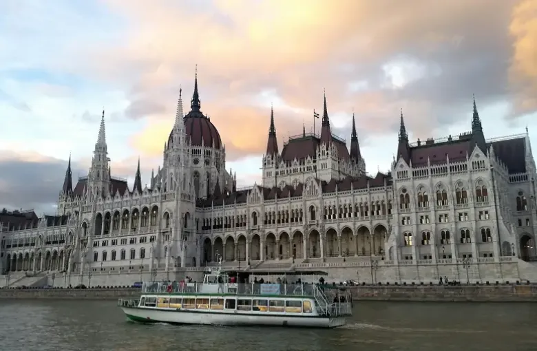 River cruise boat on the Danube passing the Hungarian Parliament Building in Budapest at sunset.