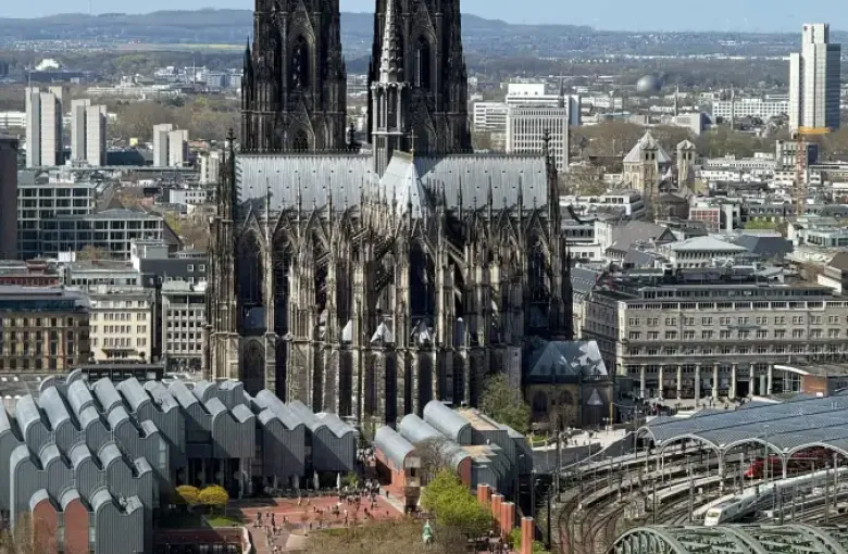 River cruise ship docked on the Rhine below Cologne Cathedral and Hohenzollern Bridge; with the city skyline beyond.