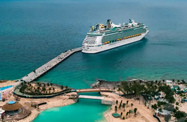 Aerial view of a Royal Caribbean cruise ship docked at a tropical island pier beside turquoise lagoon waters.