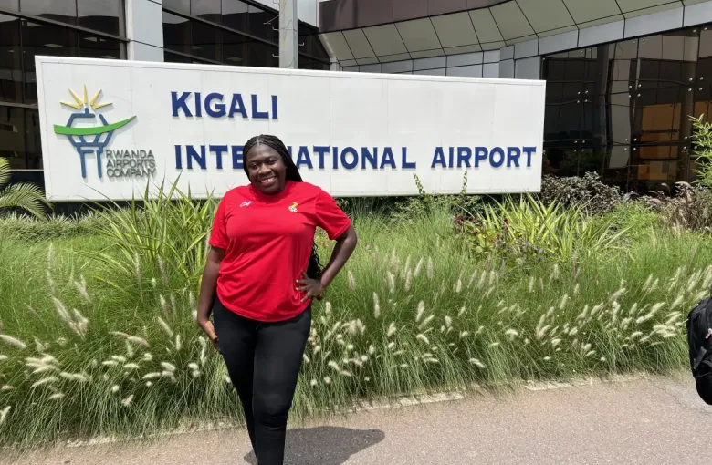 Traveler in red Ghana jersey smiling at eat-mea-2024 outside Kigali International Airport; Rwanda.
