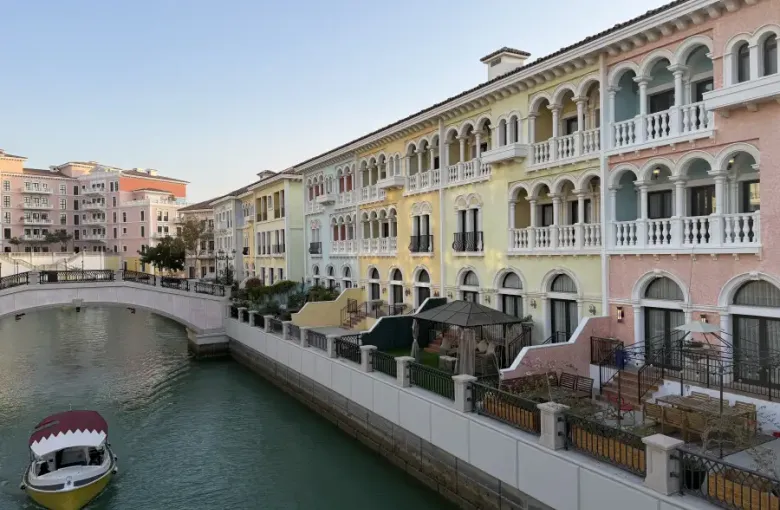 A Venetian-style canal lined with pastel buildings and a moored Qatari boat in Doha.