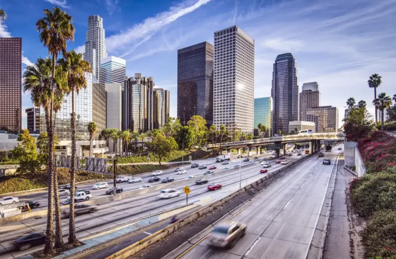 Los Angeles California downtown skyline with palm trees and multi-lane freeway traffic under a blue sky