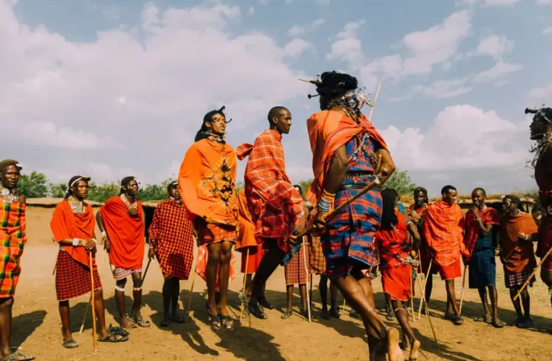Maasai warriors in vibrant red shukas perform traditional jumping dance during a cruise-land cultural village experience.