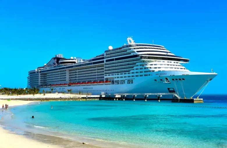 MSC Divina cruise ship docked at a tropical port with turquoise water and white sand beach under clear blue sky.