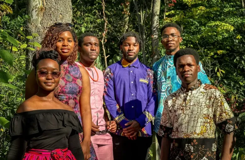Multigenerational family of six in vibrant African attire posing together among lush green trees outdoors.