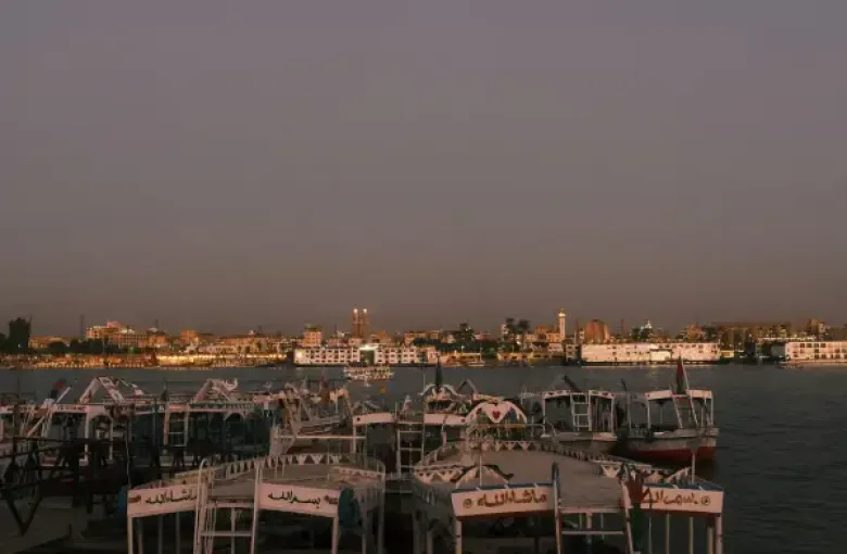 River cruise felucca boats moored on the Nile at dusk; with Luxor's illuminated skyline across the water.