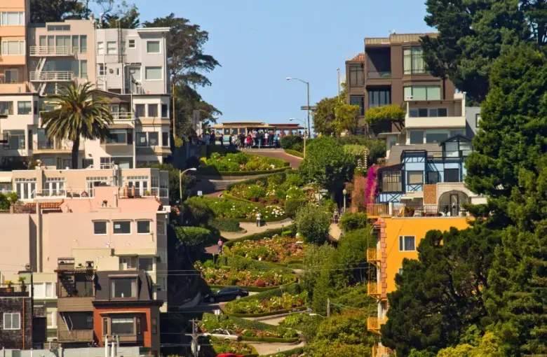 Iconic winding Lombard Street in San Francisco; CA; lined with colorful flowers; historic buildings; and a cable car at th...