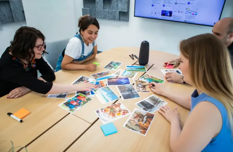 Four colleagues reviewing printed travel photos on a conference table during a travel-support planning session in a modern...