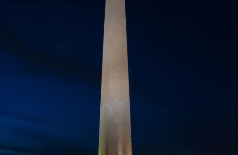 Washington DC Washington Monument illuminated at night surrounded by American flags under a deep blue sky