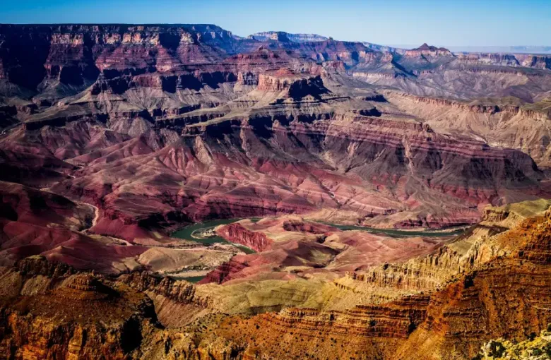 Aerial view of the Grand Canyon with the Colorado River winding through layered red rock formations.