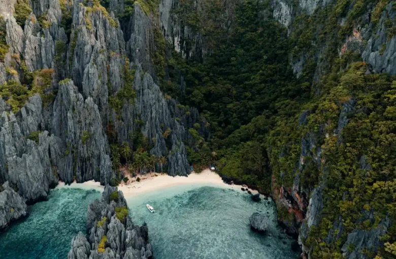 Aerial view of a secluded white-sand beach between towering limestone cliffs and turquoise water.