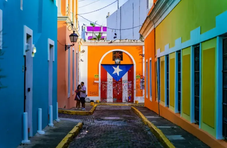 Cobblestone alley of colorful colonial buildings in Old San Juan with a Puerto Rican flag mural.