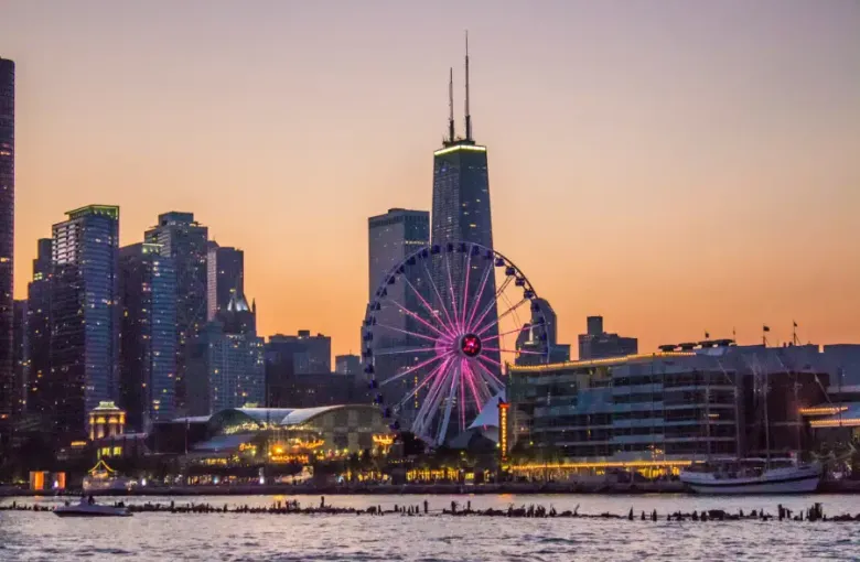Chicago's Navy Pier Ferris wheel glowing pink at sunset with the John Hancock Center and city skyline behind; viewed from...