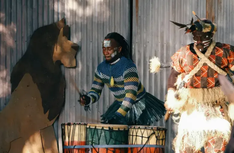 Two performers in traditional African costumes and face paint play drums on stage at an Orlando; FL cultural show.