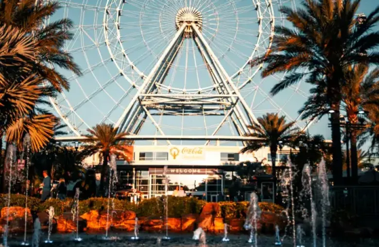The ICON Park ferris wheel rises above palm trees and fountains at dusk in Orlando; FL.