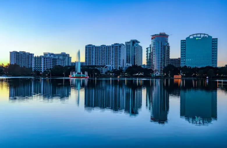 Orlando FL skyline reflecting on Lake Eola at dusk with illuminated fountain and TD Bank building visible.
