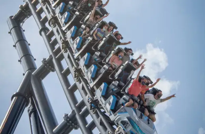 Riders with hands raised on a steep roller coaster climb at an Orlando; FL theme park on a partly cloudy day.