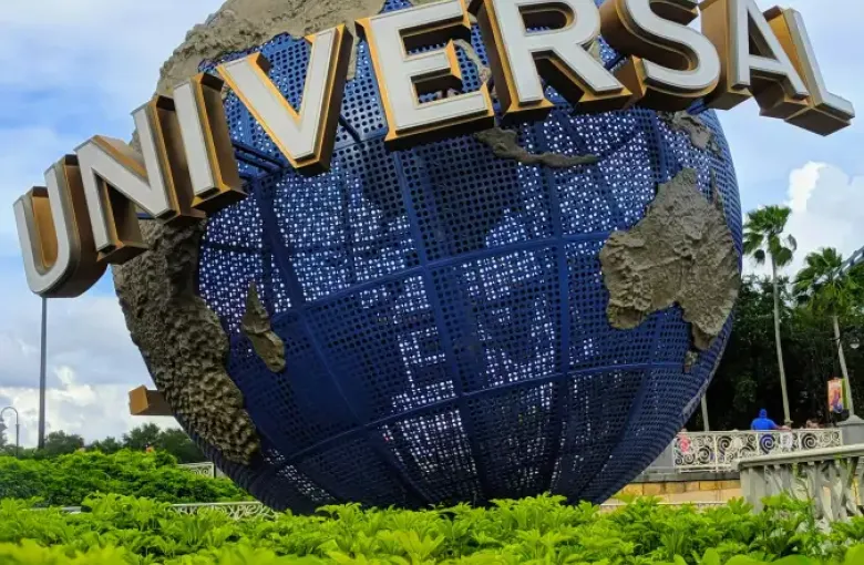 Universal Studios globe landmark at the entrance of Universal Orlando FL; surrounded by lush green hedges under a cloudy sky.