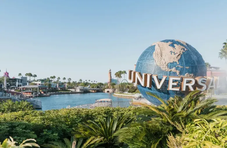 Universal Studios globe landmark beside a lagoon with palm trees and park buildings at Universal Orlando FL on a clear day.