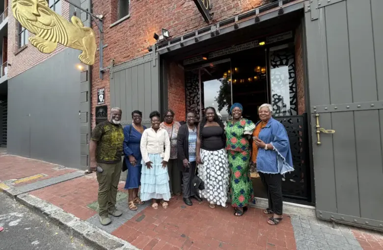 A group of eight travelers pose outside the Gold Restaurant entrance in Cape Town; South Africa; wearing colorful attire including African print fashions.