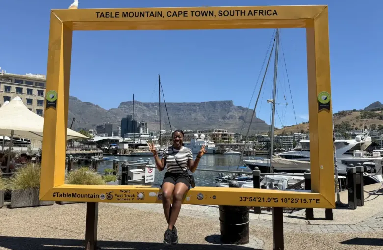 Traveler poses inside a yellow Table Mountain landmark photo frame at Cape Town's V&A Waterfront; with the iconic flat-topped mountain behind her.