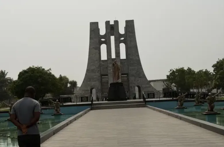 Visitor stands before the Kwame Nkrumah Memorial Park mausoleum in Accra; Ghana; with bronze statues flanking a reflective pool.