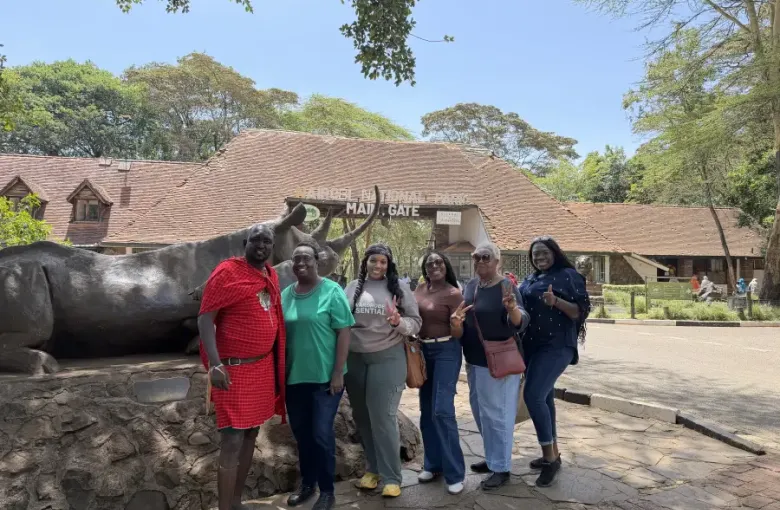 Group of six visitors posing at the Nairobi National Park Main Gate with bronze rhino sculpture in Nairobi Kenya.