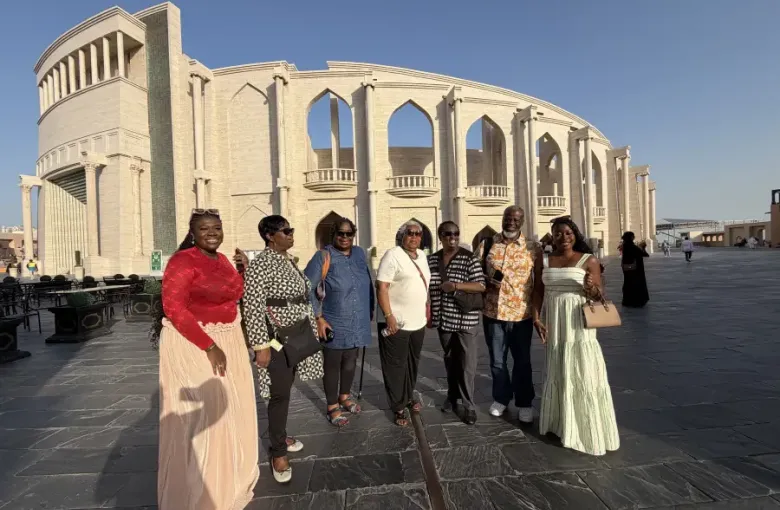 Seven travelers pose together at Katara Cultural Village in Doha Qatar; with the ornate amphitheater facade behind them.