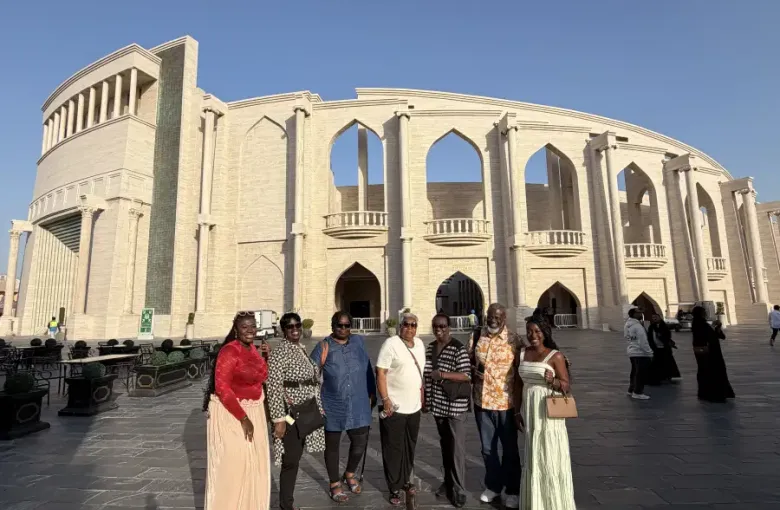 Group of seven travelers posing before a grand arched sandstone rotunda in Doha Qatar in January 2026.