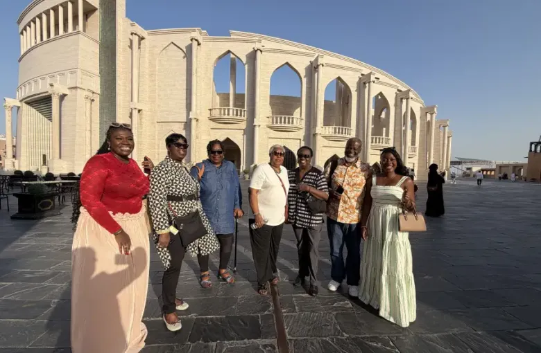 A group of seven travelers posing in front of a grand colonnaded limestone building in Doha Qatar during a January 2026 visit.