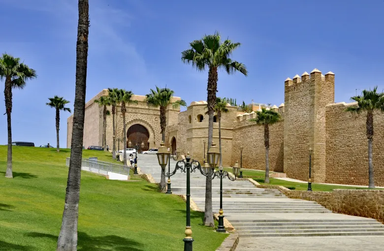 The gate and ramparts of the Kasbah of the Udayas in Rabat, framed by palms above a green lawn.