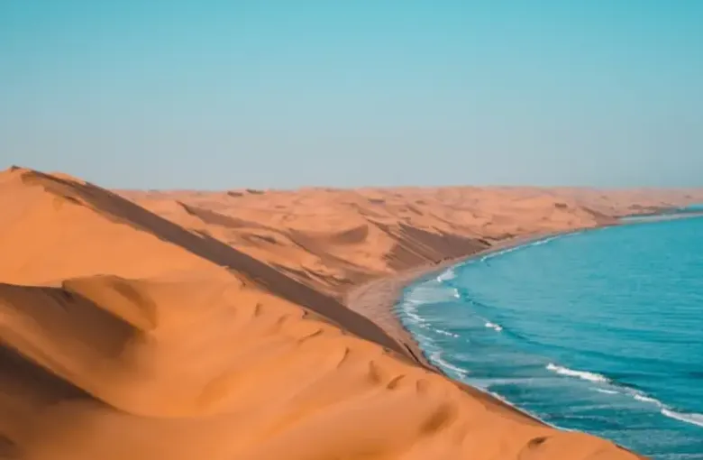 Sand dunes running straight down to meet the turquoise Atlantic along a desert coast.