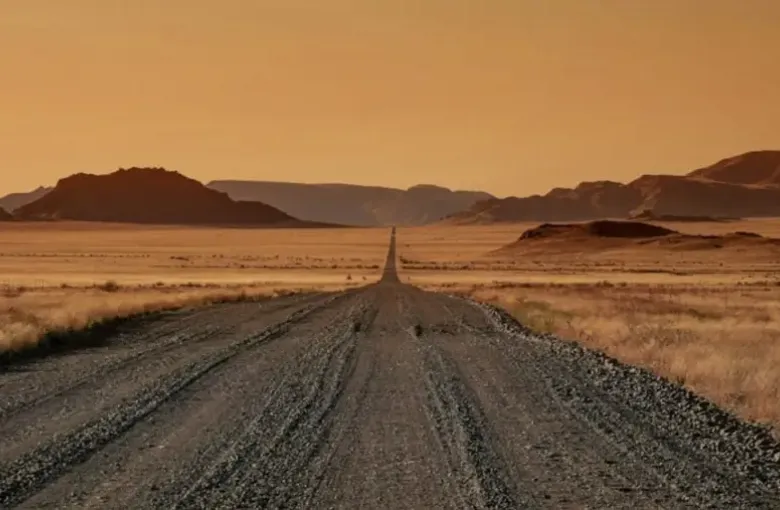 A gravel road running dead straight toward distant hills across empty desert.