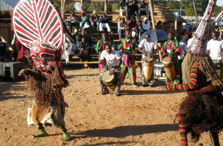 Makishi masqueraders in carved masks and costume dance before drummers at a Zambian ceremony.