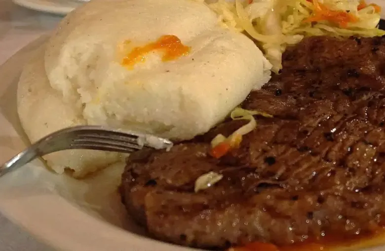 A plate of nshima served with beef relish and shredded cabbage.