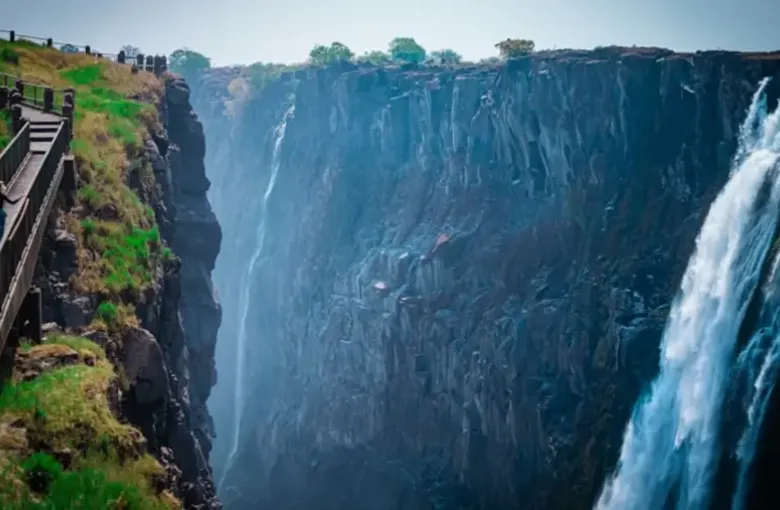 A railed viewpoint walkway overlooks the falling water of Victoria Falls on the Zambian side.