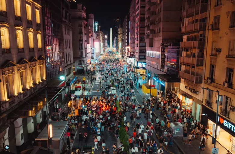 Crowds filling the pedestrianized Avenida Corrientes at night in Buenos Aires with the Obelisco lit at the far end.